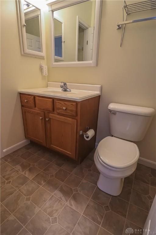 half bath with tile patterned flooring, baseboards, vanity, and toilet