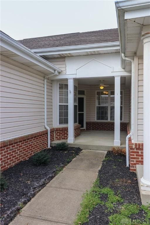 doorway to property with a porch, brick siding, and roof with shingles