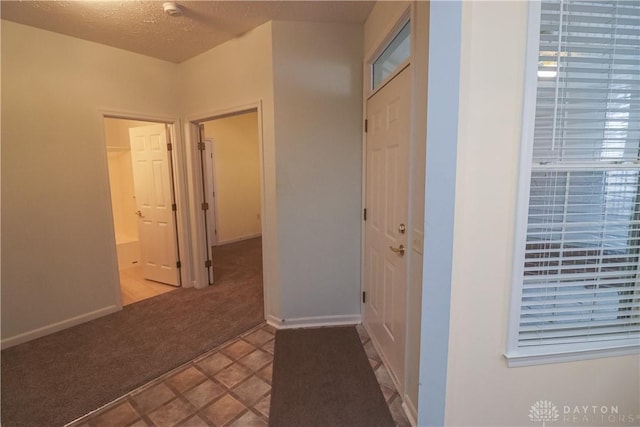 hallway with a textured ceiling, carpet floors, and baseboards