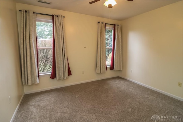 carpeted spare room featuring ceiling fan, visible vents, and baseboards