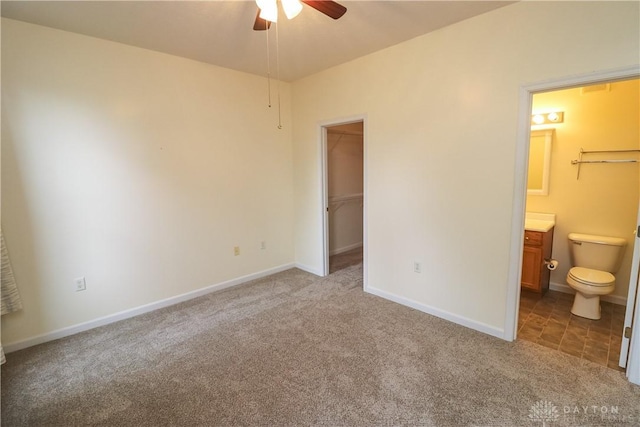 unfurnished bedroom featuring carpet, a walk in closet, connected bathroom, and baseboards