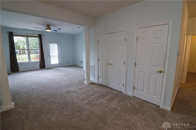 unfurnished bedroom featuring carpet floors, visible vents, baseboards, multiple closets, and decorative columns