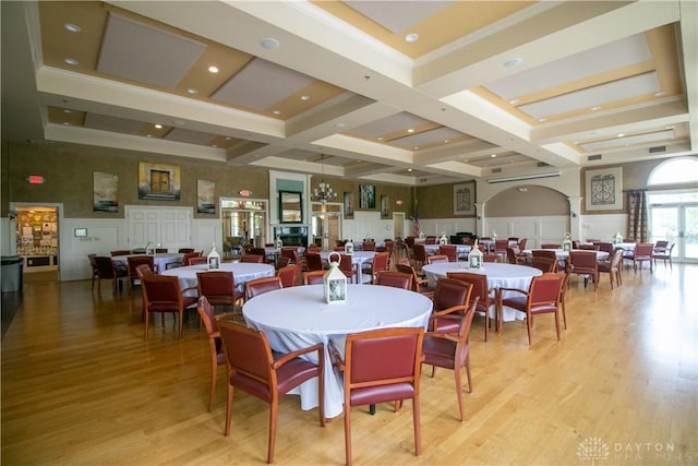 dining area featuring light wood-type flooring, coffered ceiling, a decorative wall, and ornate columns