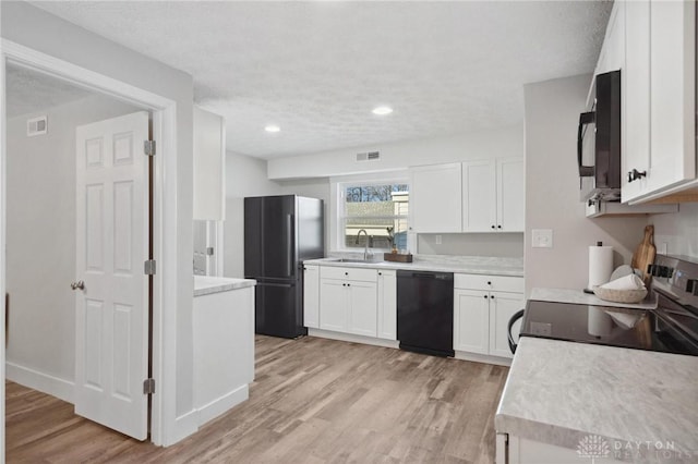 kitchen featuring sink, a textured ceiling, white cabinets, black appliances, and light wood-type flooring