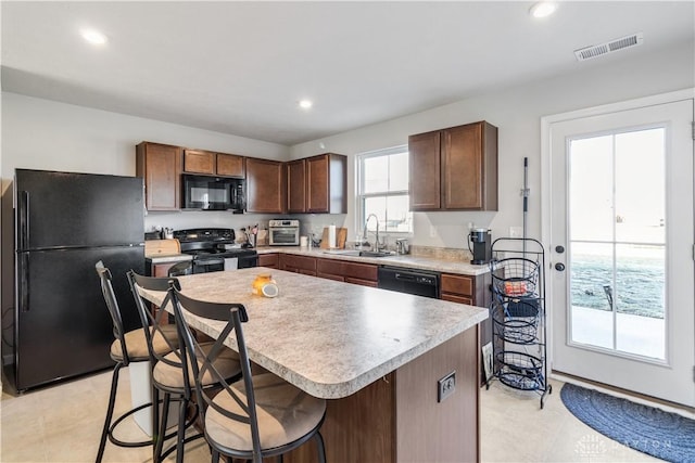 kitchen with black appliances, a kitchen island, sink, light tile patterned flooring, and a breakfast bar