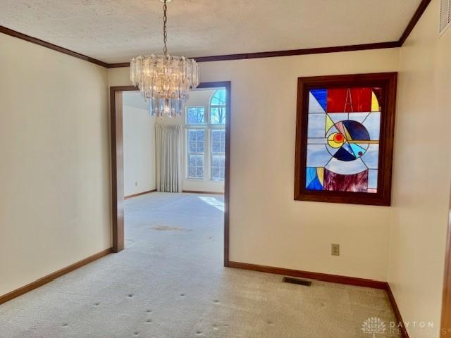 unfurnished dining area with carpet flooring, ornamental molding, a textured ceiling, and an inviting chandelier