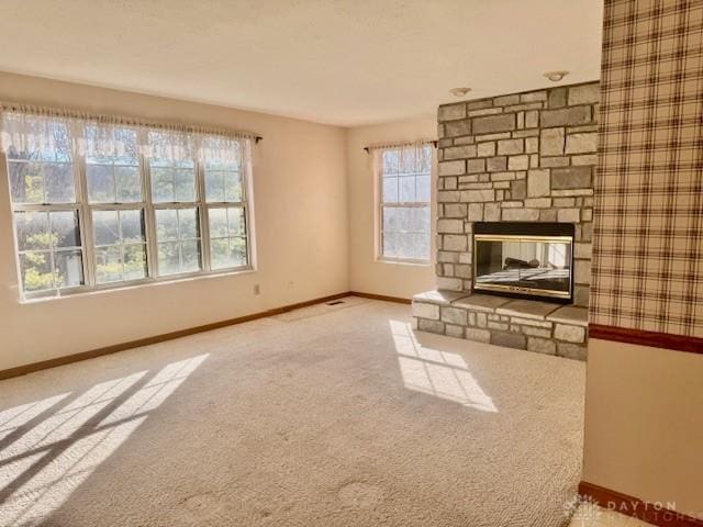 unfurnished living room featuring a stone fireplace, light carpet, and plenty of natural light