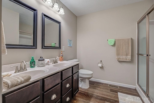 bathroom featuring wood-type flooring, vanity, an enclosed shower, toilet, and a textured ceiling