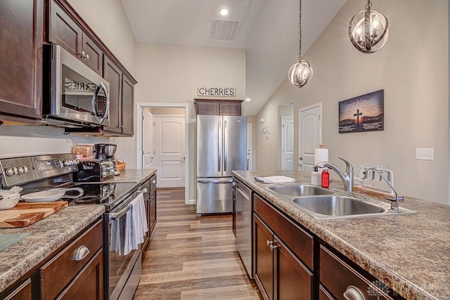 kitchen featuring sink, hanging light fixtures, stainless steel appliances, dark brown cabinetry, and vaulted ceiling