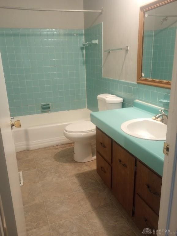 full bathroom featuring vanity, tiled shower / bath, tile patterned flooring, toilet, and tile walls