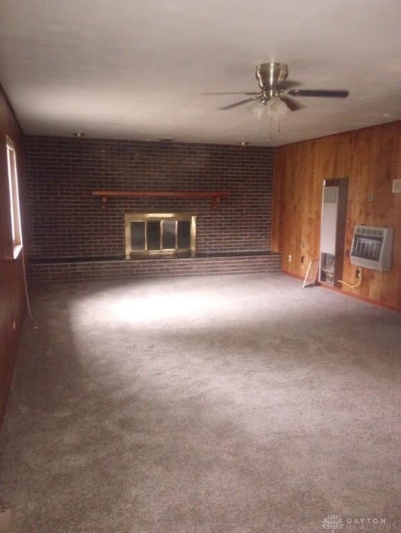 empty room featuring carpet flooring, heating unit, wood walls, and a fireplace