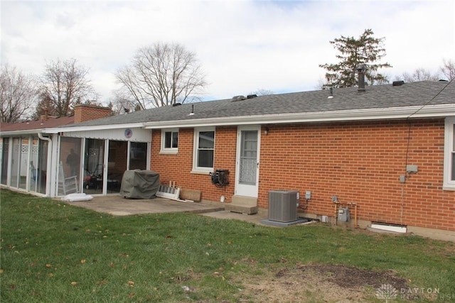 rear view of property with a sunroom, a chimney, central air condition unit, a lawn, and brick siding