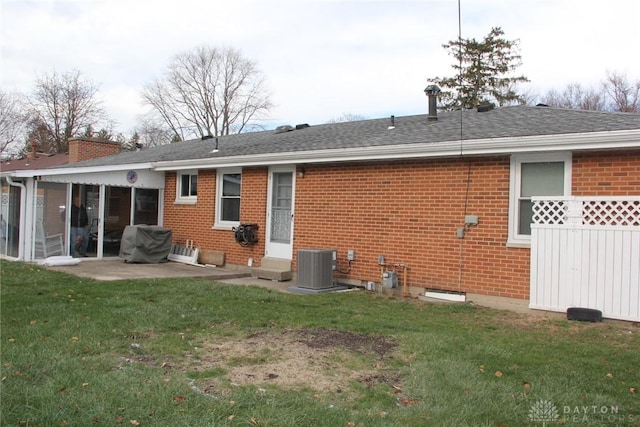 rear view of house with roof with shingles, a yard, central AC, a patio area, and brick siding