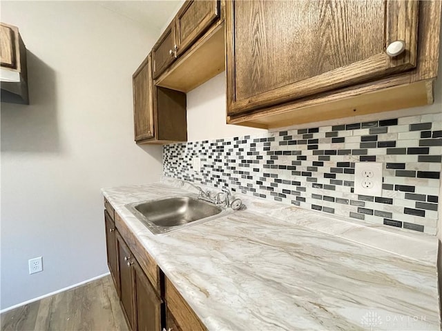 kitchen featuring wood finished floors, baseboards, a sink, light countertops, and backsplash