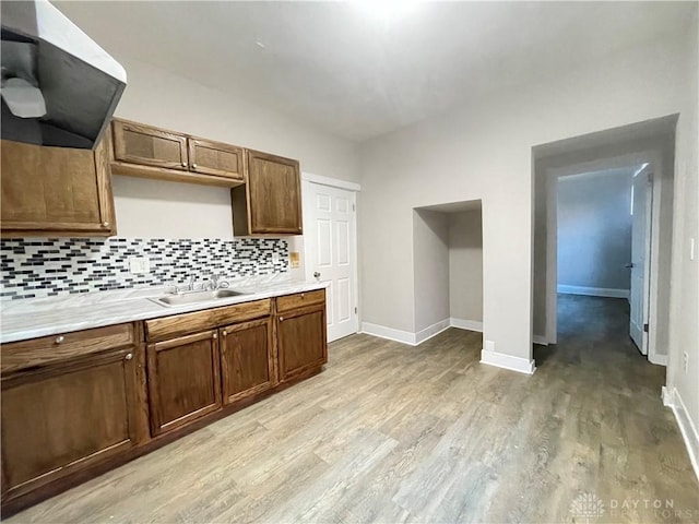 kitchen with tasteful backsplash, extractor fan, light countertops, light wood-style floors, and a sink