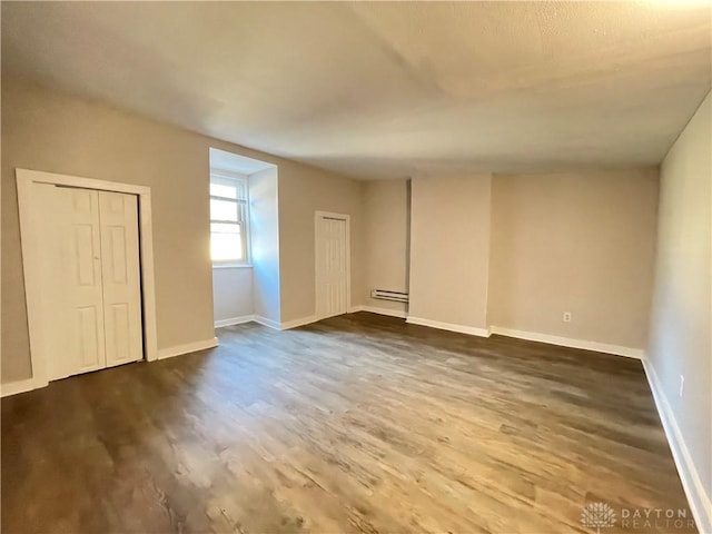 spare room with a baseboard radiator, baseboards, and dark wood-style flooring