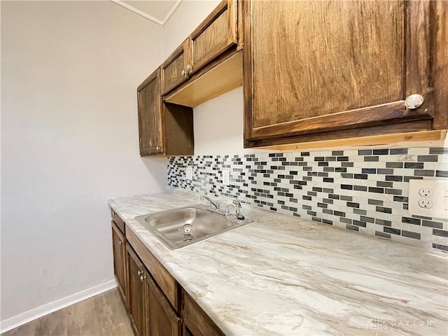 kitchen with baseboards, light countertops, decorative backsplash, light wood-style flooring, and a sink