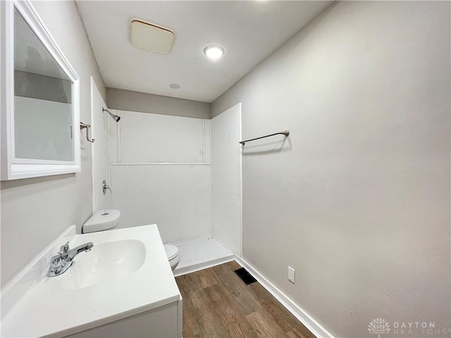 bathroom with a shower, toilet, wood finished floors, and vanity