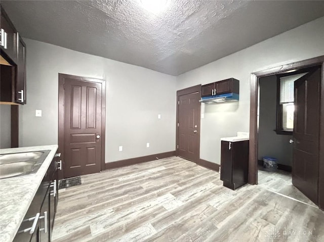 kitchen with a textured ceiling, light hardwood / wood-style floors, dark brown cabinetry, and sink