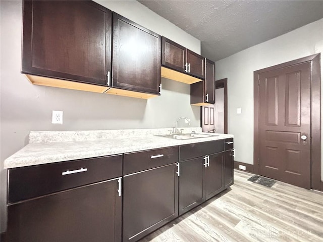 kitchen with a textured ceiling, dark brown cabinets, sink, and light hardwood / wood-style flooring