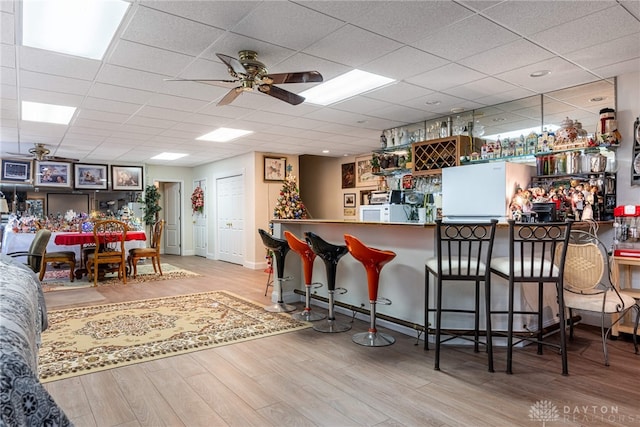 kitchen featuring ceiling fan, a drop ceiling, light hardwood / wood-style flooring, kitchen peninsula, and a breakfast bar area