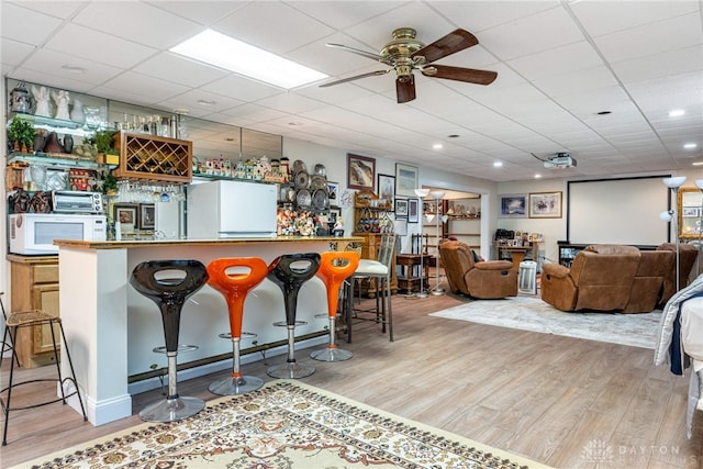 bar featuring light wood-type flooring, white appliances, ceiling fan, and a paneled ceiling