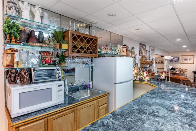 kitchen featuring a drop ceiling, white appliances, and sink