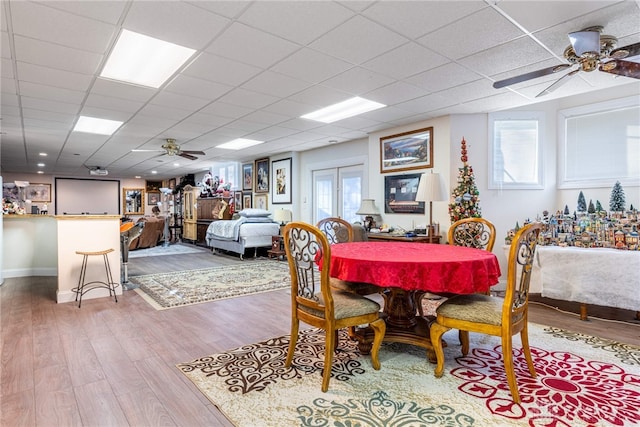 dining space featuring wood-type flooring, a drop ceiling, and ceiling fan