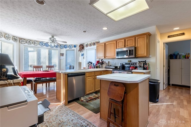 kitchen with appliances with stainless steel finishes, a center island, a textured ceiling, and light hardwood / wood-style flooring