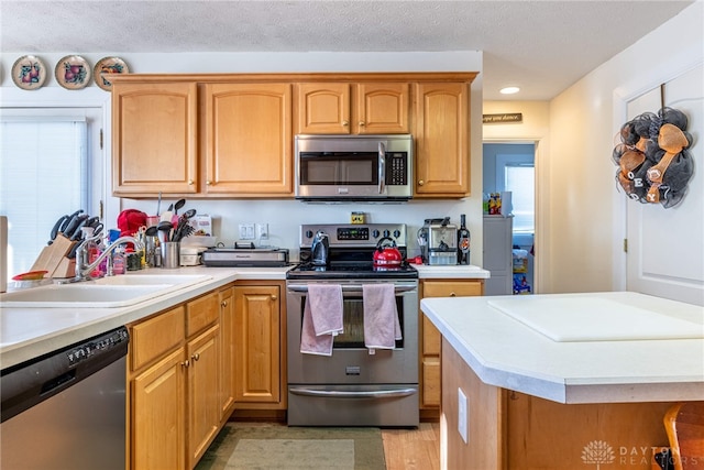 kitchen featuring a textured ceiling, sink, light wood-type flooring, and stainless steel appliances