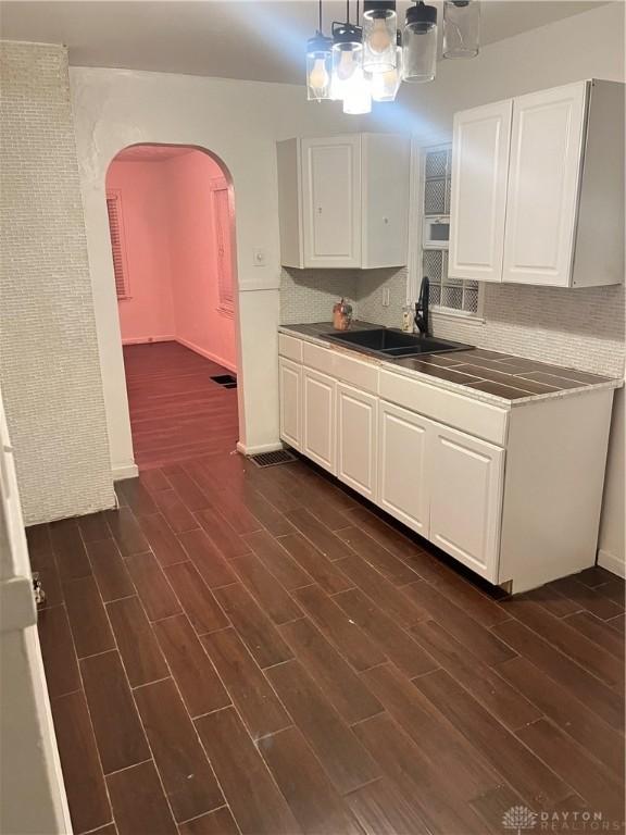 kitchen with decorative backsplash, dark wood-type flooring, sink, decorative light fixtures, and white cabinets