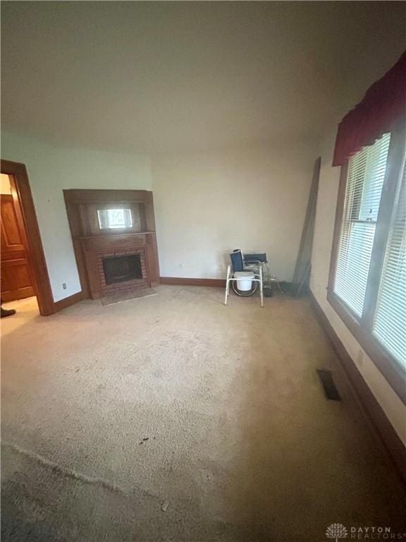 unfurnished living room with light carpet and a brick fireplace