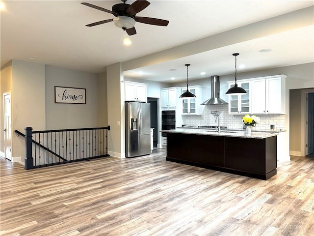 kitchen featuring white cabinetry, an island with sink, wall chimney range hood, and appliances with stainless steel finishes