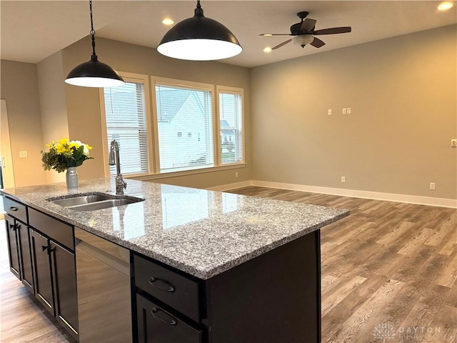 kitchen featuring light stone countertops, sink, decorative light fixtures, dishwasher, and an island with sink