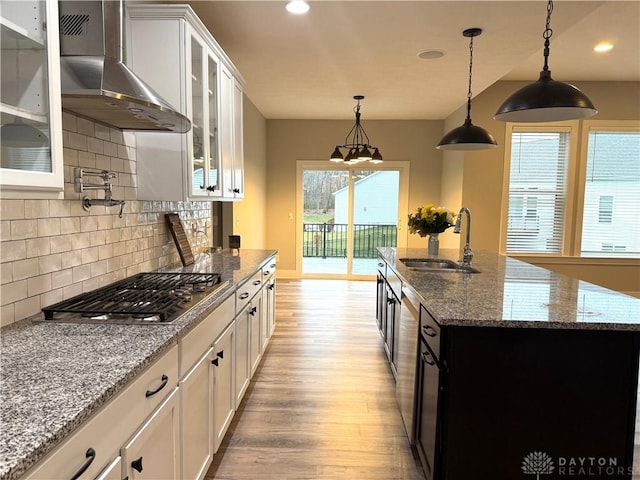 kitchen with a center island with sink, sink, wall chimney exhaust hood, light wood-type flooring, and white cabinetry