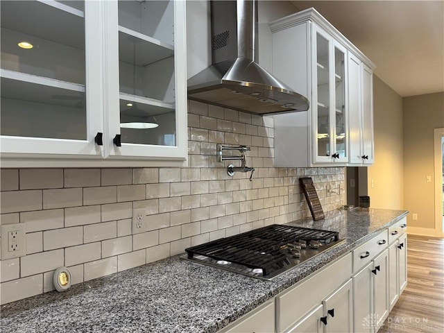 kitchen featuring wall chimney exhaust hood, tasteful backsplash, stainless steel gas stovetop, white cabinets, and light wood-type flooring