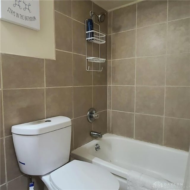 bathroom featuring tiled shower / bath combo, toilet, and tile walls