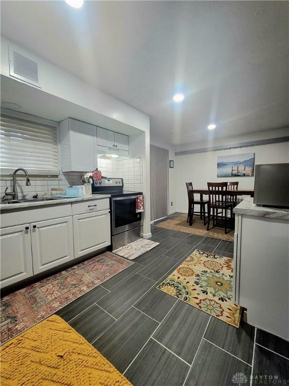 kitchen with white cabinets, backsplash, stainless steel electric range oven, and sink