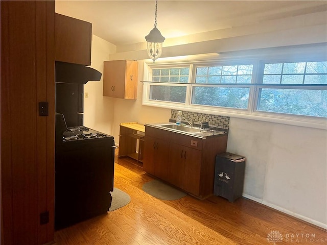 kitchen with range with gas cooktop, under cabinet range hood, a sink, light wood-type flooring, and hanging light fixtures