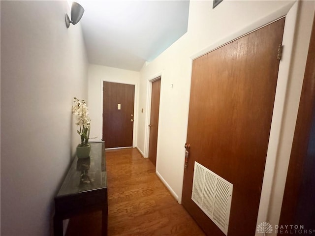 hall featuring baseboards, visible vents, and wood finished floors