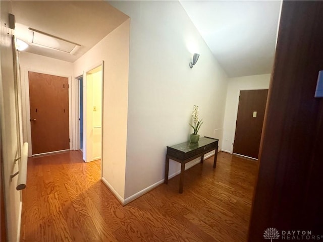corridor featuring baseboards, wood finished floors, and attic access