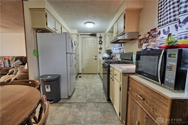 kitchen with a textured ceiling, white refrigerator, black range with gas cooktop, and cream cabinetry