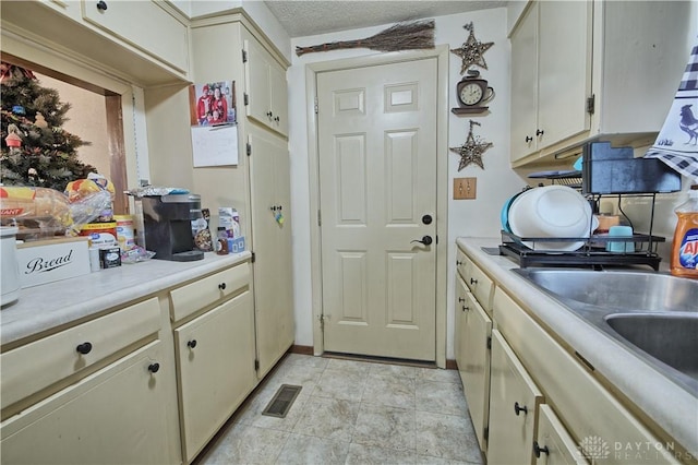 kitchen with sink, a textured ceiling, and cream cabinets