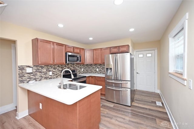 kitchen featuring kitchen peninsula, stainless steel appliances, light hardwood / wood-style flooring, and tasteful backsplash