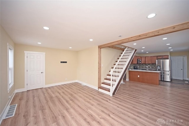 basement featuring stainless steel fridge with ice dispenser, light hardwood / wood-style floors, and sink