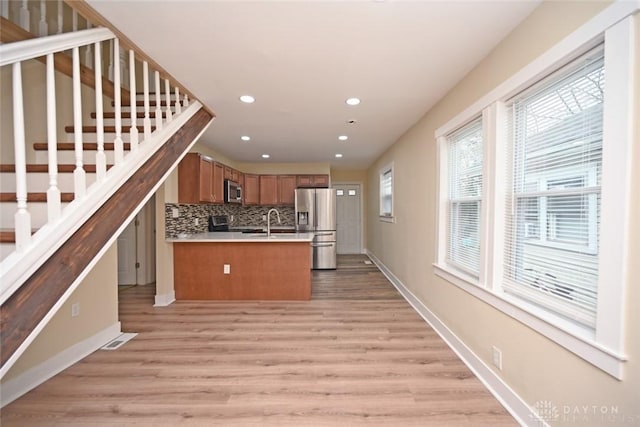 kitchen with kitchen peninsula, backsplash, stainless steel appliances, and light hardwood / wood-style flooring