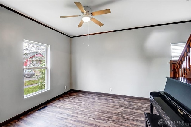 unfurnished room featuring dark wood-type flooring, a wealth of natural light, ornamental molding, and ceiling fan