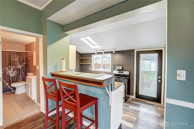 kitchen with a breakfast bar, stainless steel range with gas stovetop, white cabinets, and light hardwood / wood-style flooring