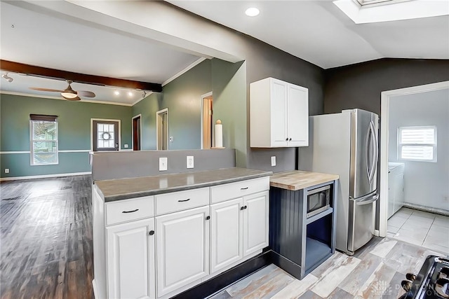 kitchen with stainless steel appliances, white cabinetry, lofted ceiling with skylight, and wooden counters