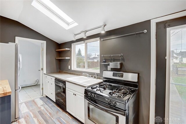 kitchen featuring vaulted ceiling with skylight, stainless steel appliances, sink, light hardwood / wood-style flooring, and white cabinets